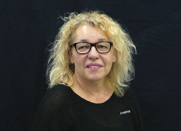 Catherine Holliger vom Verkaufsinnendienst, verantwortlich für Bestellungen, Rechnungen und Buchhaltung, posiert vor einem schwarzen Hintergrund.