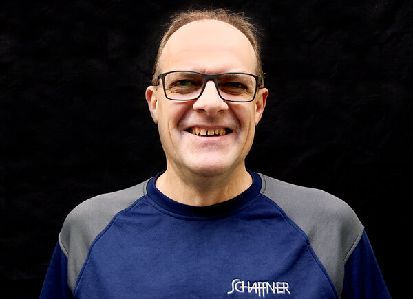 Daniel Wullschleger, Leiter der Farbproduktion, posiert lächelnd vor einem schwarzen Hintergrund im Schaffner GF AG-Shirt.
