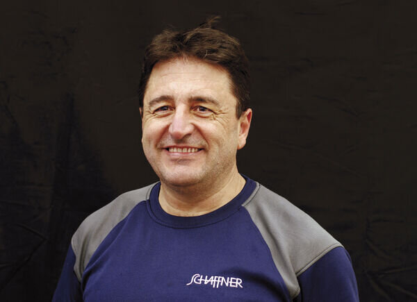 Tamer Sentuerk, Mitarbeiter im Logistikbereich, posiert vor einem schwarzen Hintergrund in einem Schaffner GF AG-T-Shirt.